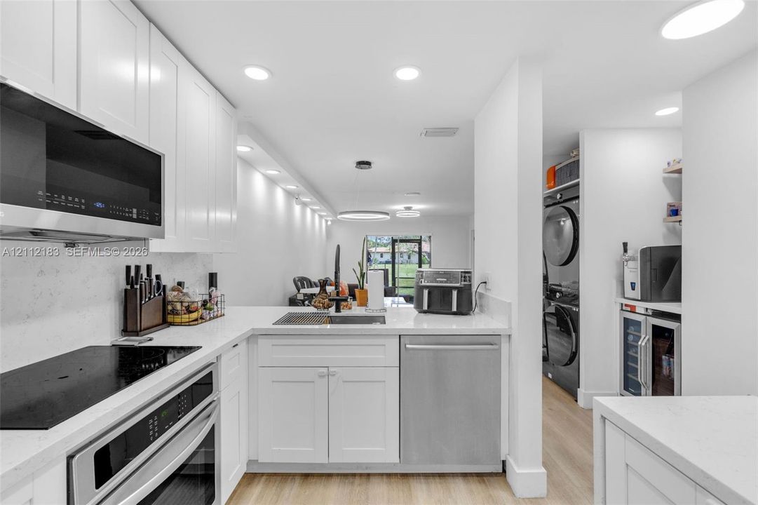 Kitchen featuring white shaker-style cabinetry, solid-surface countertops, recessed lighting, and stainless steel appliances, including an integrated dishwasher and a built-in beverage refrigerator