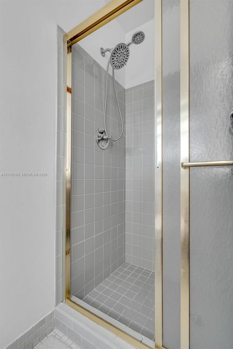 Shower stall featuring grey square tile wall and floor surround, gold-finish frame, and dual-head shower fixture