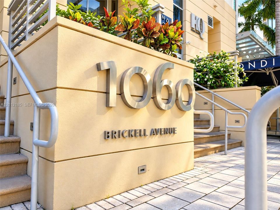 Exterior building signage featuring raised metallic house numbers, integrated stucco masonry, paved stone hardscaping, and recessed wall-mounted lighting