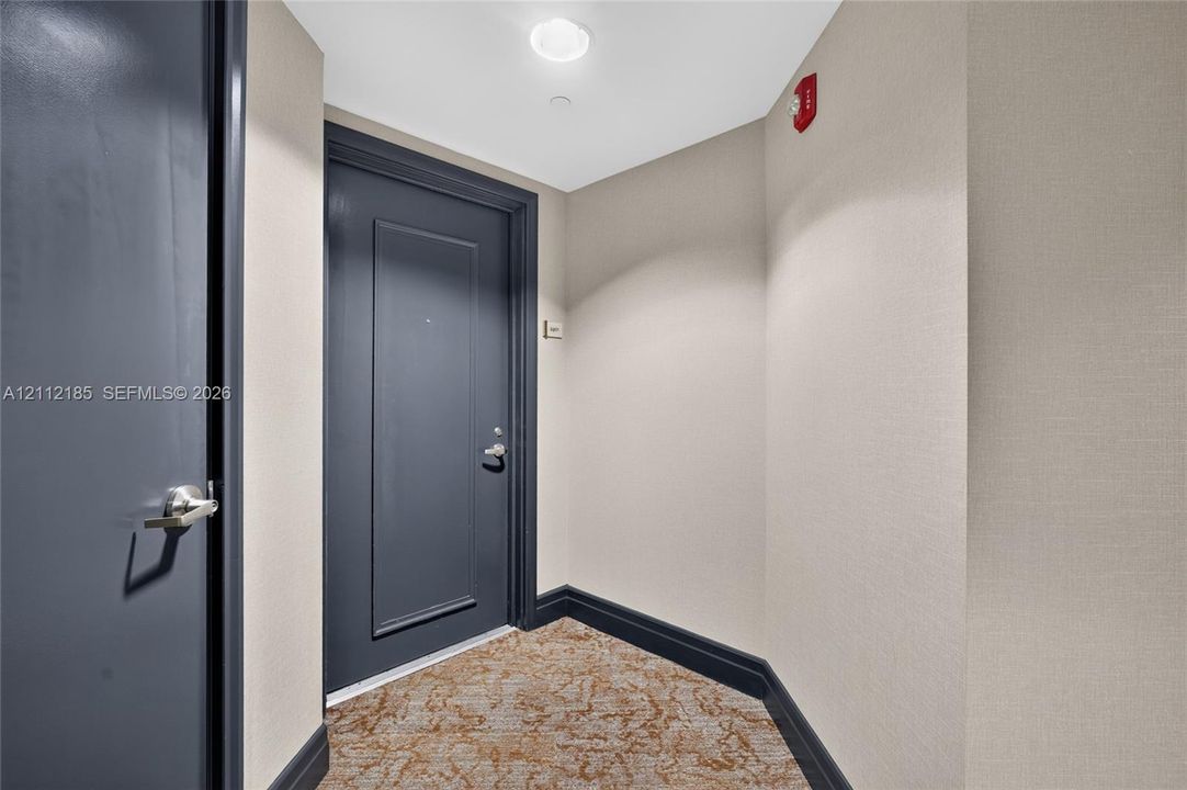 Entryway featuring dark-finish paneled doors, neutral textured wall coverings, and patterned carpeting with bold trim detailing