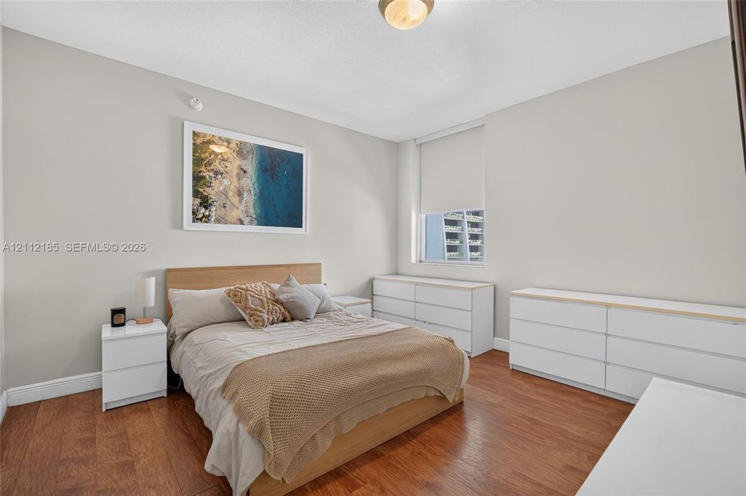 Room interior featuring wood-finish flooring, neutral wall tones, and a window with a roller shade