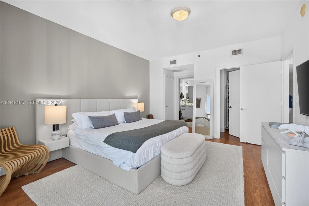 Neutral-toned room featuring wood-finish flooring, a contemporary floating headboard with integrated side tables, and multiple interior door access points