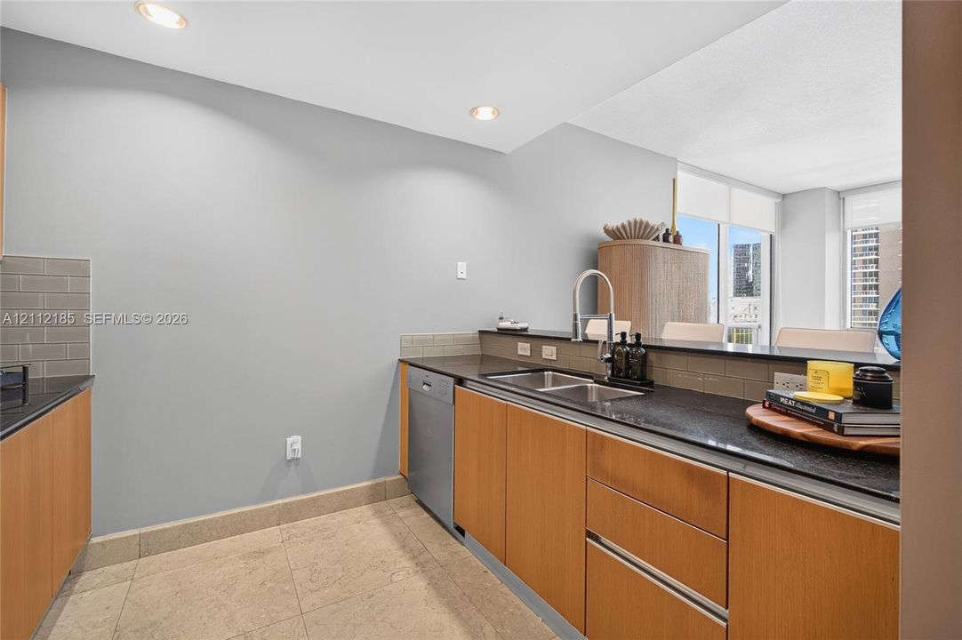 Kitchen featuring flat-panel wood cabinetry, dark stone countertops, an undermount double-basin sink with a high-arch faucet, integrated dishwasher, and tile backsplash
