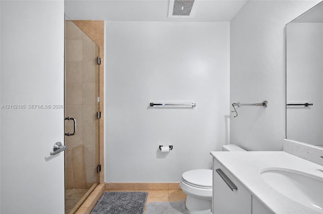 Bathroom featuring a frameless glass-enclosed shower with tile surround, a white vanity with a composite countertop, an undermount sink, and a wall-mounted mirror