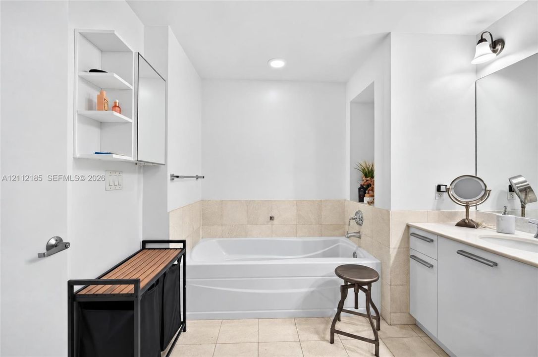 Bathroom featuring a deep soaking tub with neutral tile surround, built-in shelving, vanity with integrated basin, and polished chrome hardware