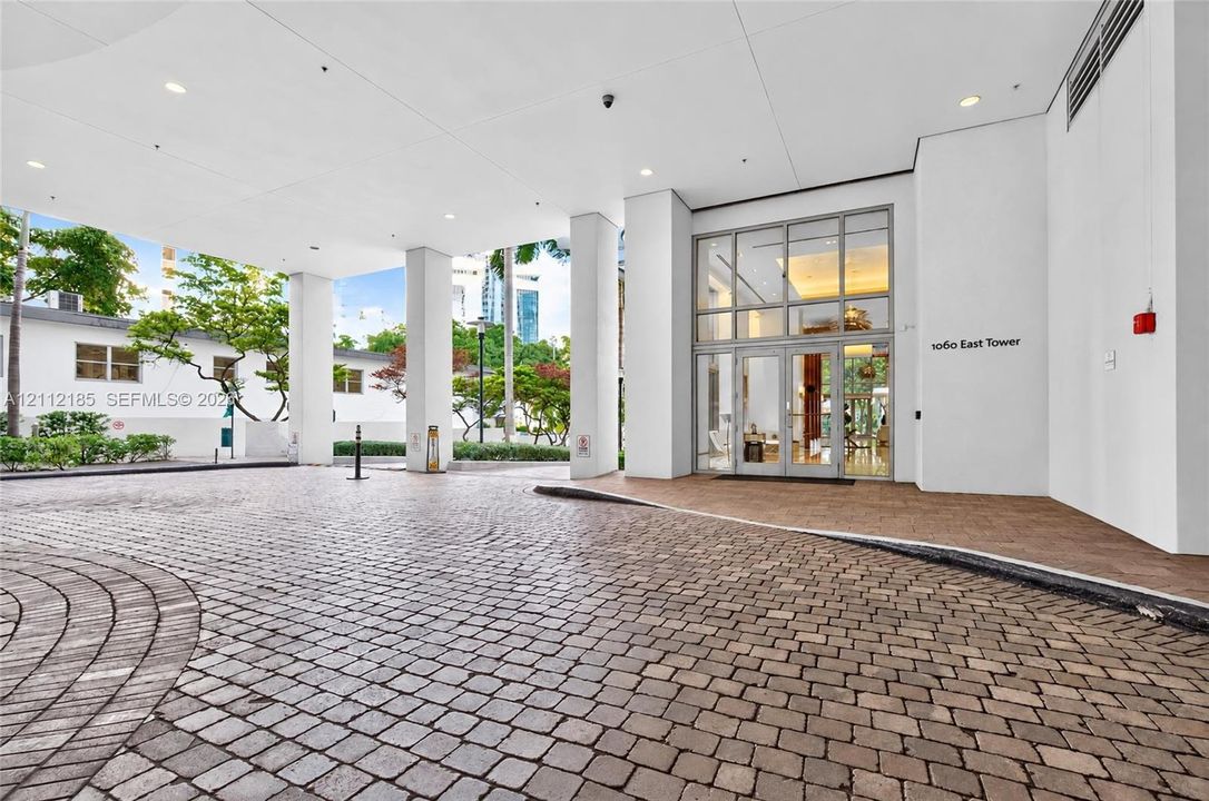 Covered motor court entrance featuring stone paver driveway, glass-paneled double entry doors, high ceilings with recessed lighting, and support columns