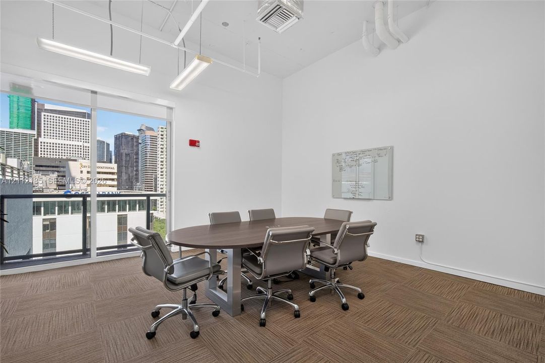 Open-concept space featuring floor-to-ceiling windows, urban skyscraper backdrop, high ceilings, linear pendant lighting, and modular carpet tiling