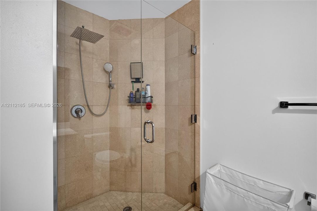 Walk-in shower featuring tile walls, a frameless glass enclosure, a square rainfall showerhead, and a handheld shower wand