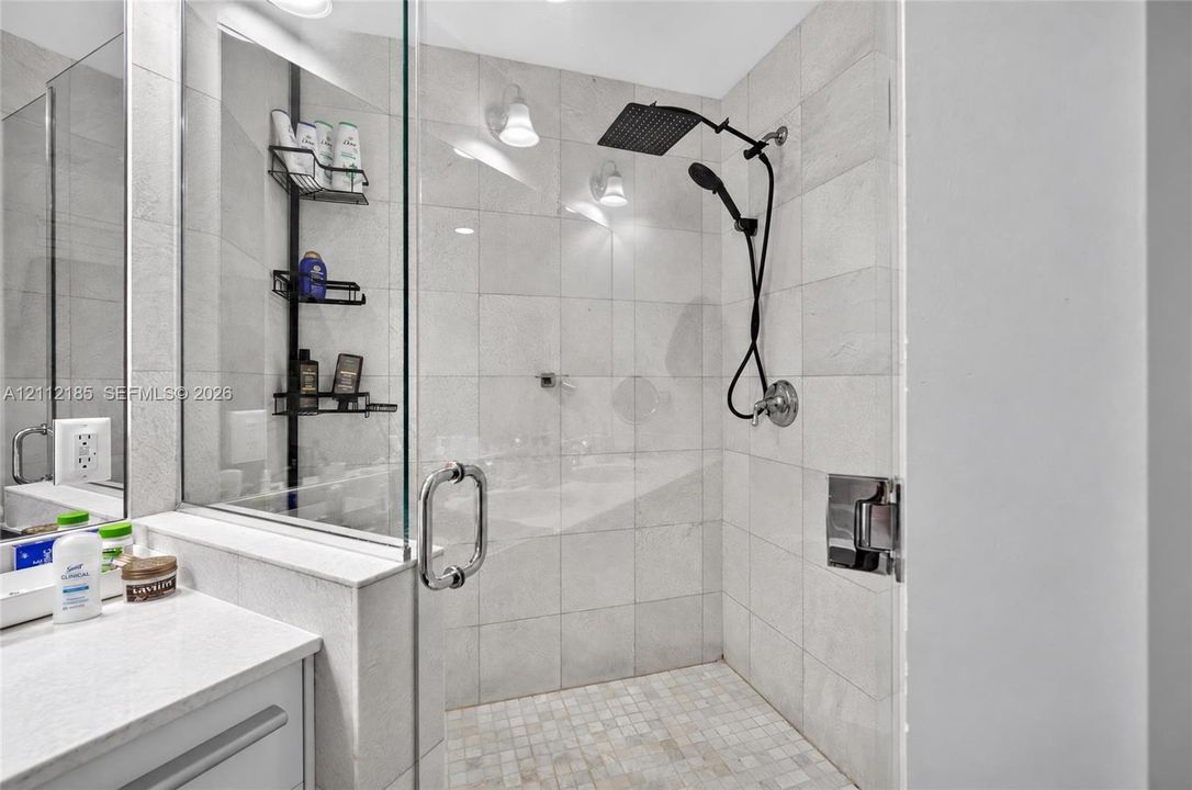 Walk-in shower featuring light-toned tile wall surround, mosaic tile floor, glass enclosure, and dual-function matte black showerhead