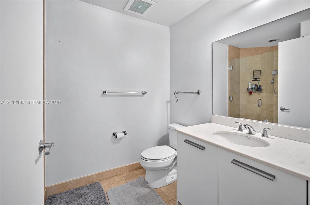 Bathroom featuring a white vanity with a stone countertop and undermount sink, large wall-mounted mirror, and a glass-enclosed shower with stone tile surround