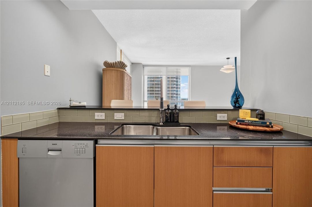 Kitchen featuring flat-panel wood-finish cabinetry, dark solid-surface countertops, a stainless steel dual-basin undermount sink, and a subway tile backsplash