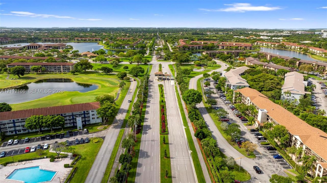 Aerial perspective of a multi-building community featuring multiple water features, manicured green space, paved parking areas, and an outdoor swimming pool