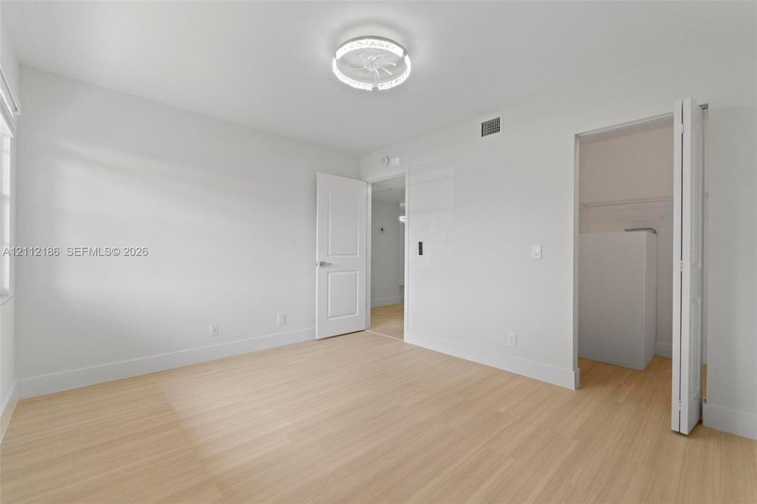 Light-toned wood-finish flooring, crisp neutral wall paint, modern ceiling-mounted lighting fixture, and interior doors with integrated closets