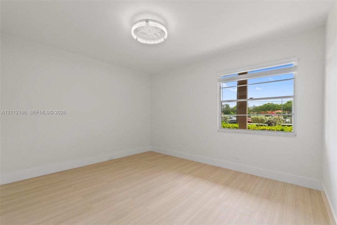 Light-filled room featuring wood-finish flooring, crisp neutral walls, and a modern circular LED flush-mount fixture