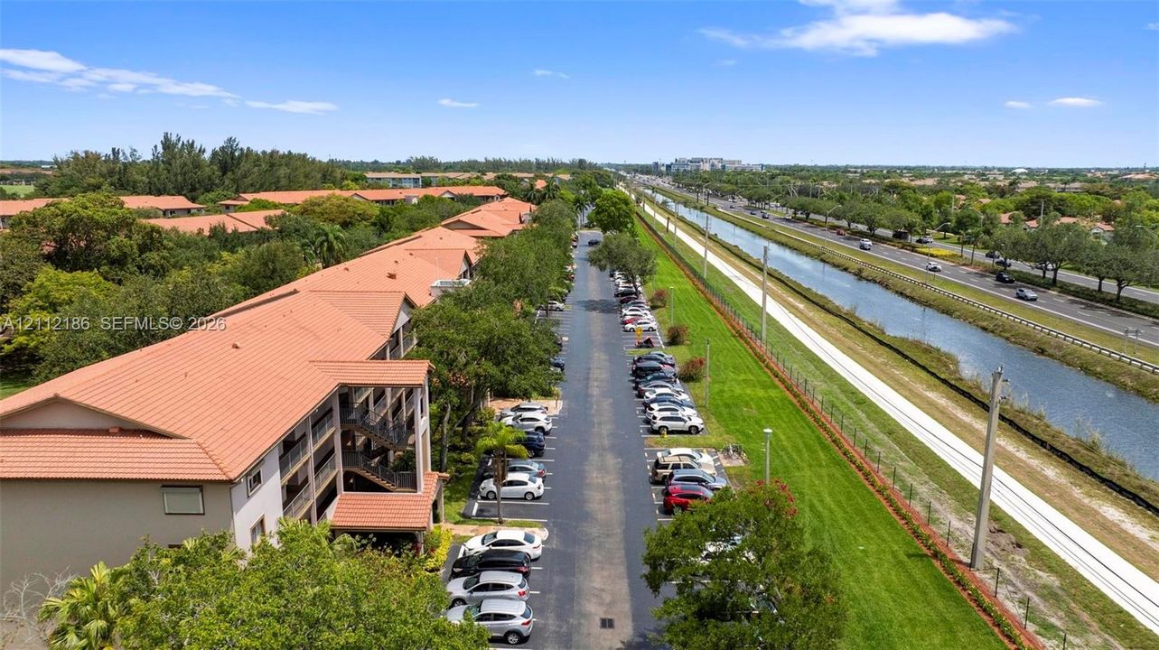 Aerial perspective featuring a multi-story building with clay-tile roofing, dedicated asphalt parking, and expansive grassy grounds bordering a waterway