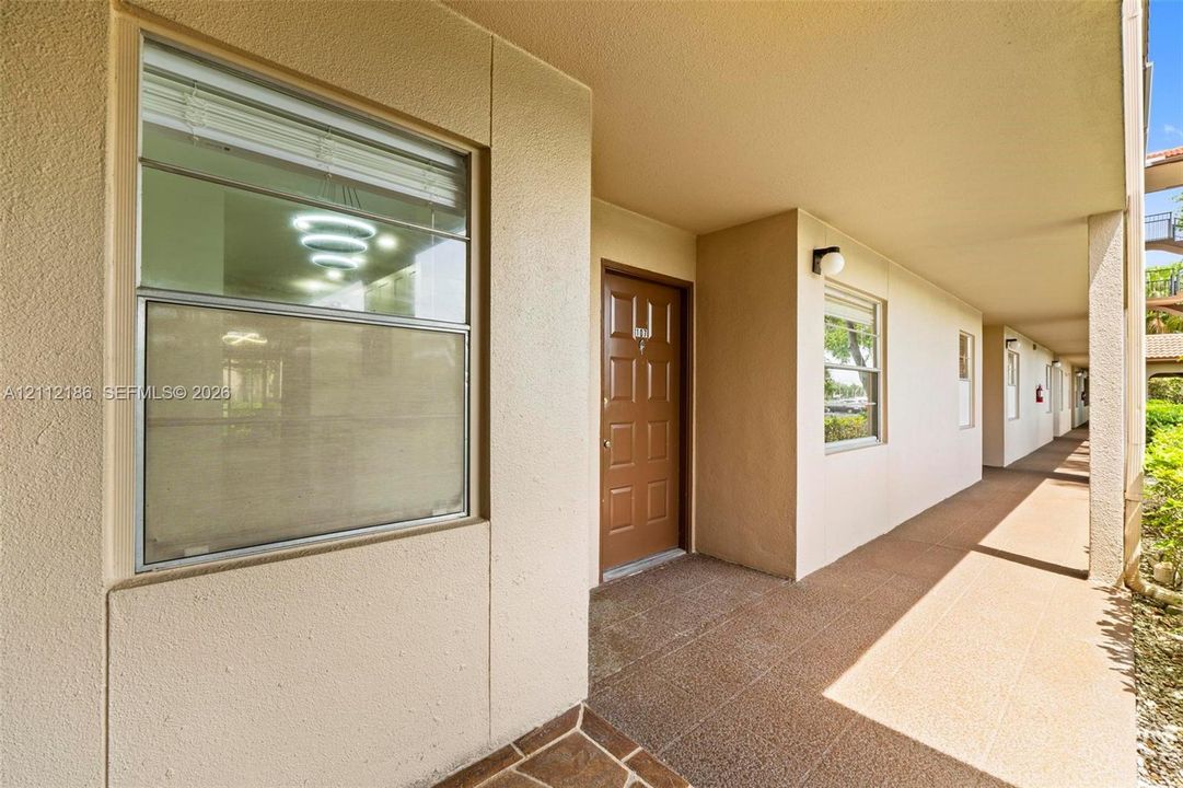 Covered walkway featuring a paneled entry door, dual-pane windows, and textured exterior finish