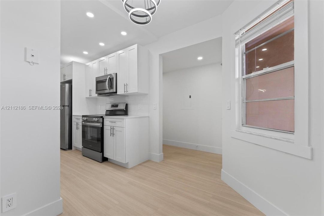 Kitchen featuring white Shaker-style cabinetry, stainless steel appliances, light-toned wood-finish flooring, recessed lighting, and a modern circular chandelier