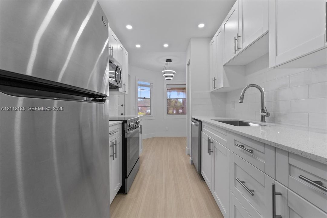 Kitchen featuring white shaker-style cabinetry, quartz countertops, stainless steel appliances, white subway tile backsplash, and light-toned wood-finish flooring