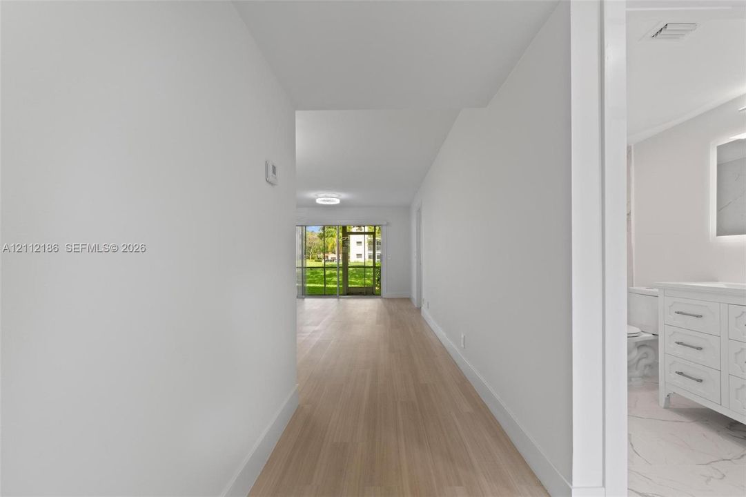 Interior hallway featuring light-toned wood-finish flooring and a bathroom vanity with a lighted mirror