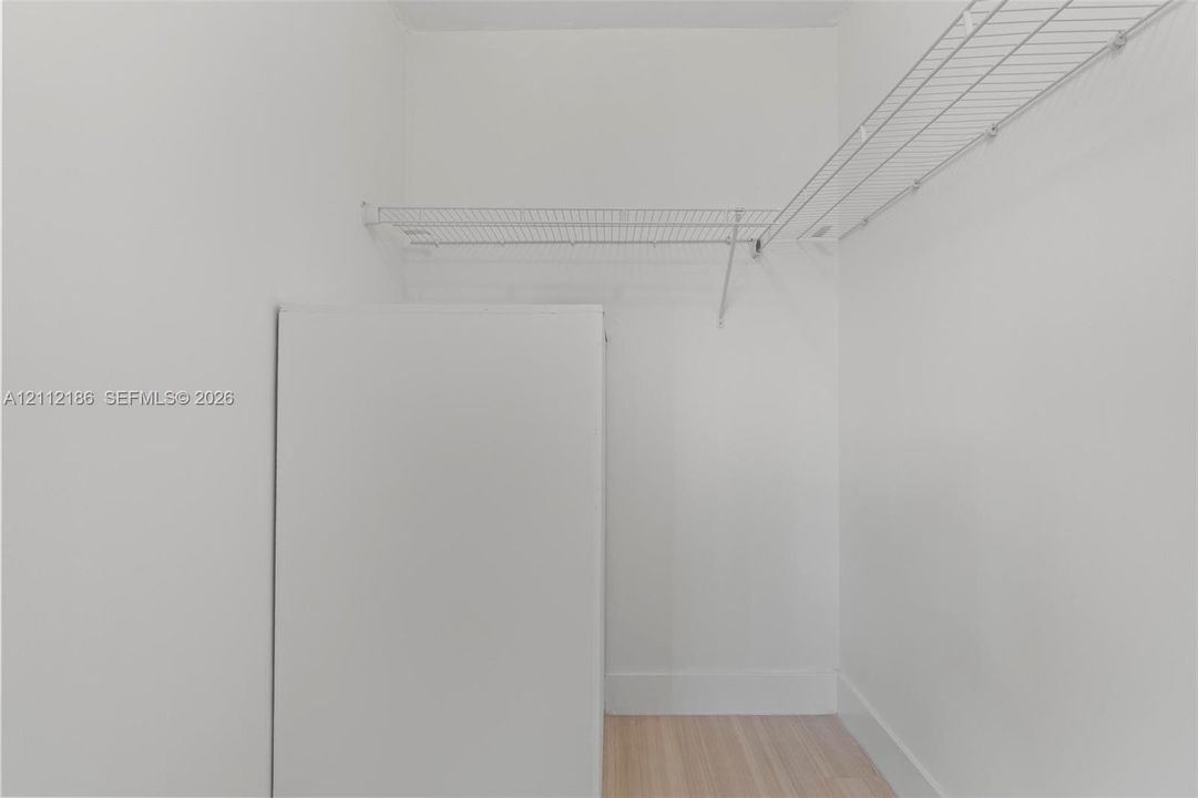 Storage area featuring white walls, wood-finish flooring, and integrated white wire shelving