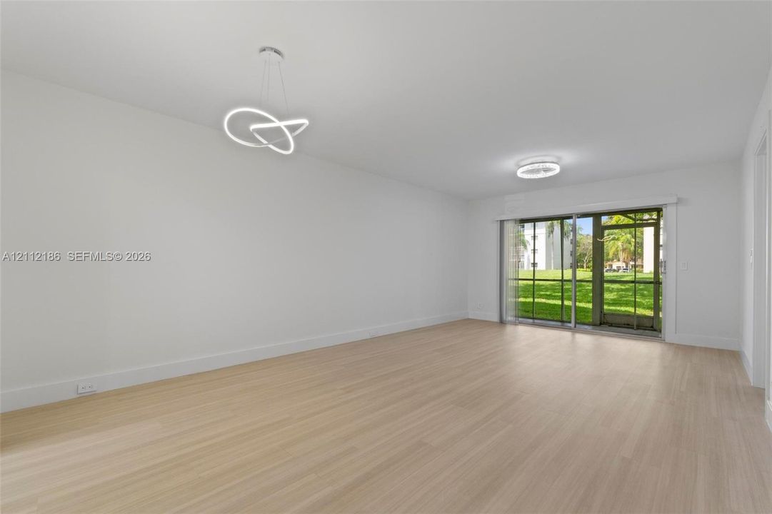 Open-concept interior featuring light wood-finish flooring, modern geometric LED pendant lighting, and a sliding glass door providing external access