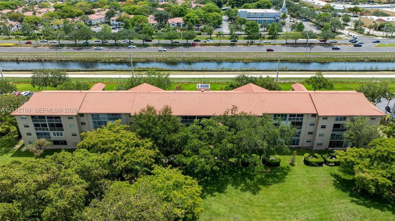 Multi-story building featuring a tile roof, screened-in balcony enclosures, and expansive surrounding green space with mature trees