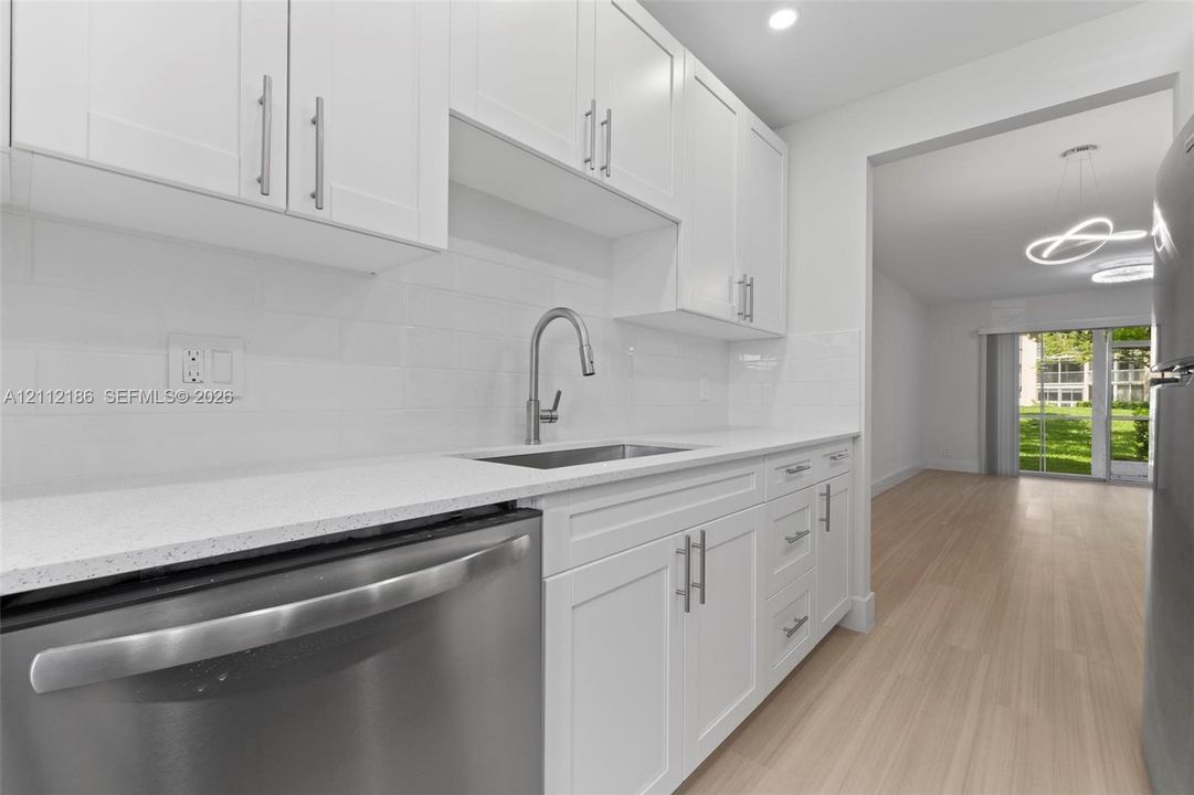 Kitchen featuring white shaker-style cabinetry, quartz countertops, subway tile backsplash, stainless steel appliances, and wood-finish flooring