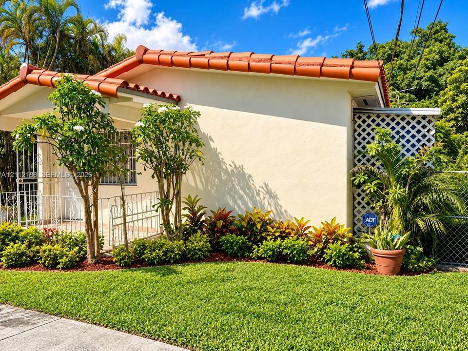 Stucco exterior featuring a terracotta tile roof, decorative metal front door security screen, and landscaped garden beds