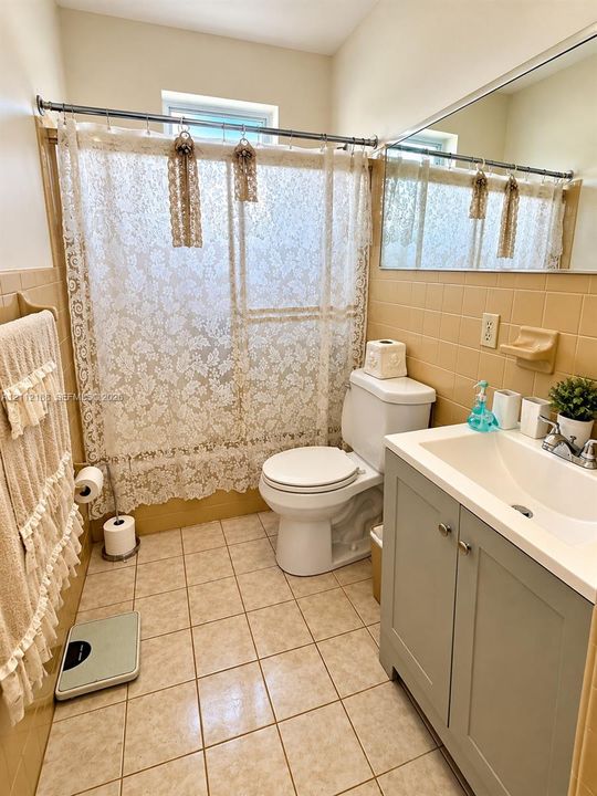 Bathroom featuring square tile flooring, wall-mounted mirror, vanity cabinet with integrated sink, and tile-surround shower area