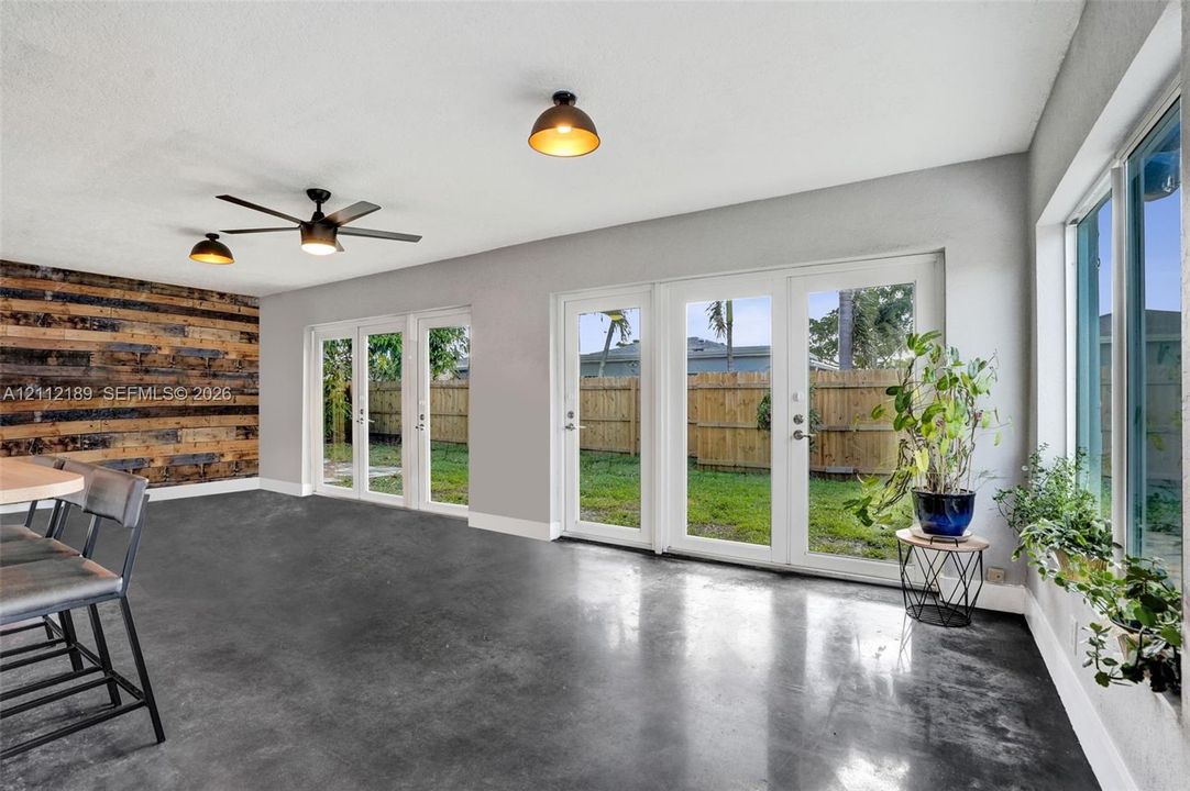 Polished concrete flooring, accent wall with horizontal wood planks, multiple sets of white-framed glass doors, and modern industrial-style ceiling fixtures