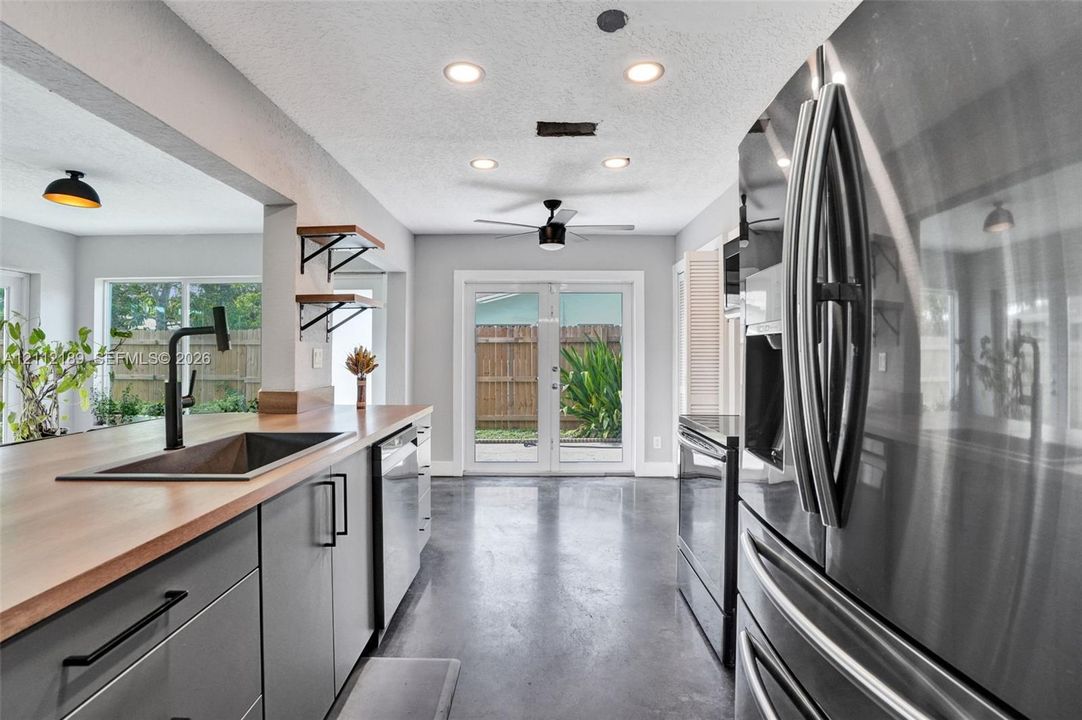 Kitchen featuring grey flat-panel cabinetry, wood-surface countertops, a matte black faucet with an undermount sink, stainless steel appliances, and polished concrete flooring