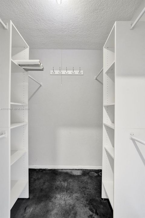 Walk-in closet featuring white built-in shelving, dual hanging rods, and a wall-mounted hook rack