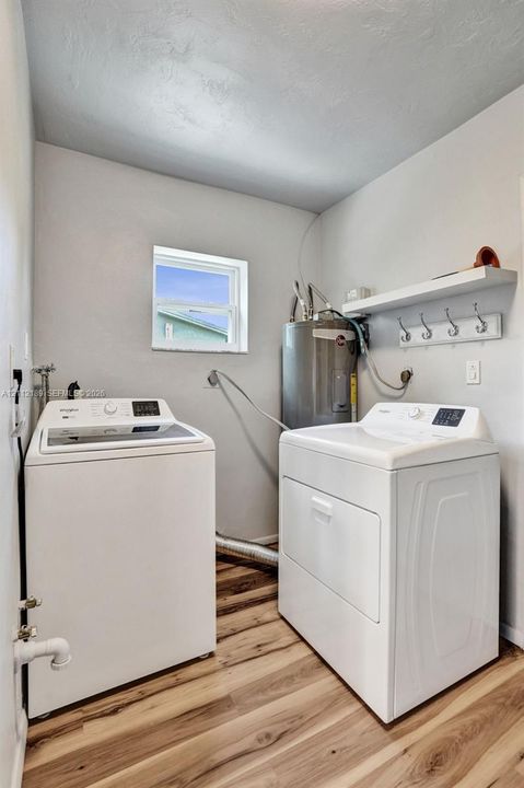 Laundry area featuring wood-finish flooring, a built-in wall shelf with a row of coat hooks, and a dedicated water heater