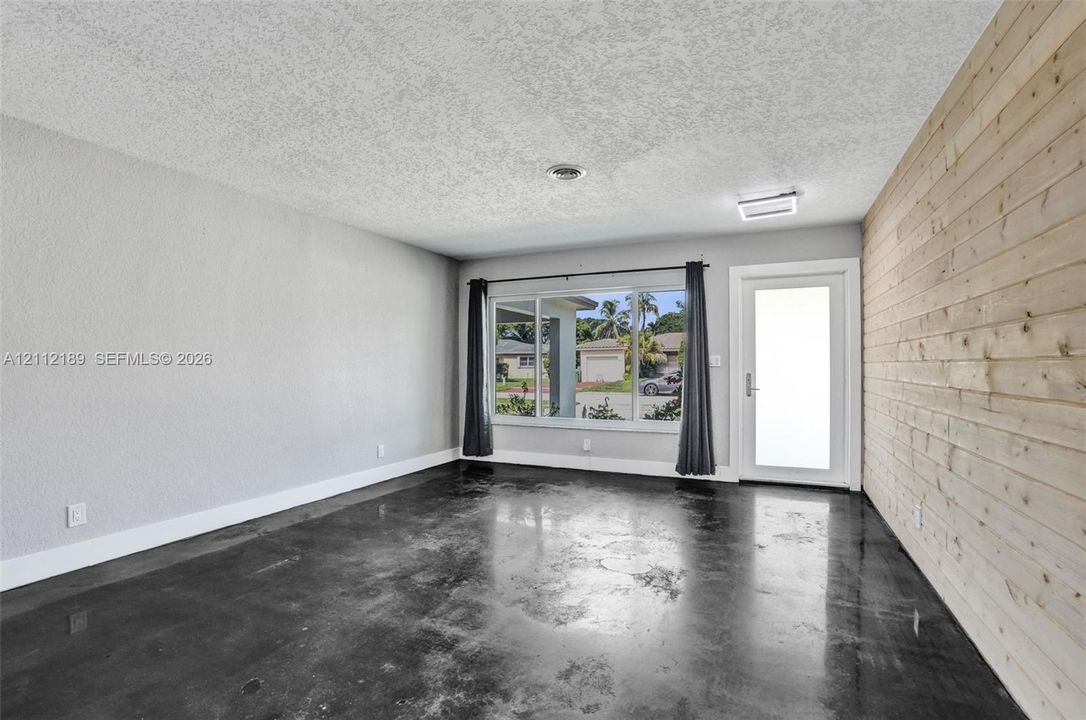 Polished concrete flooring, horizontal wood-plank accent wall, large picture window, and exterior door with frosted glass insert