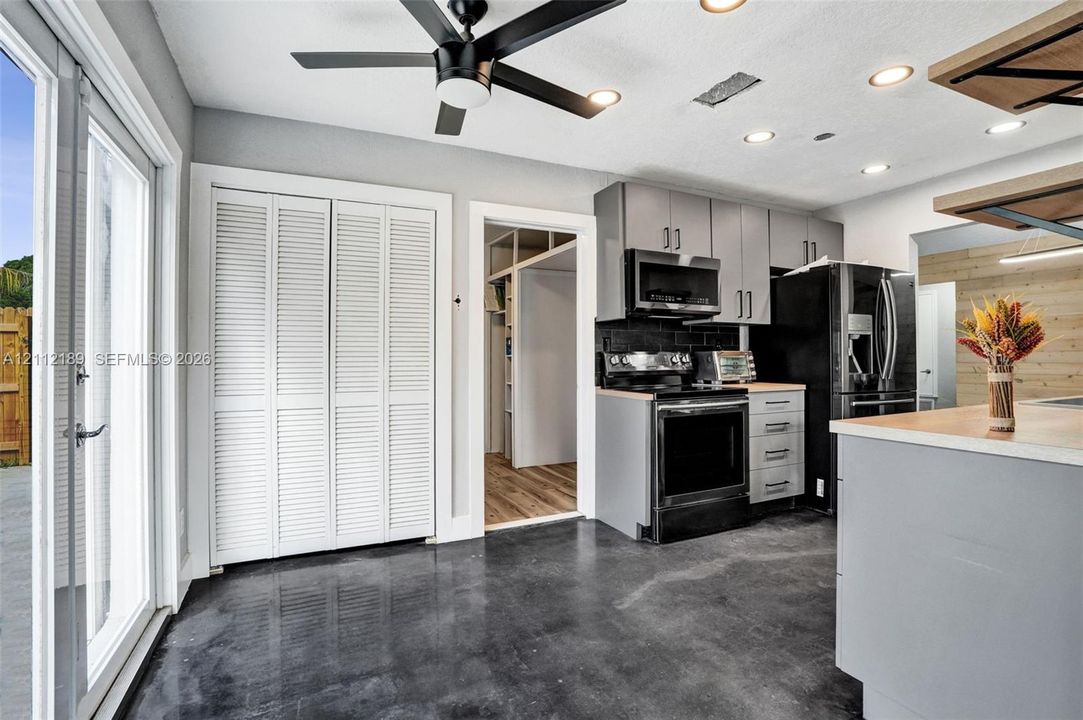 Kitchen featuring charcoal-toned cabinetry, stainless steel appliances, polished concrete flooring, a ceiling fan, and double glass patio doors