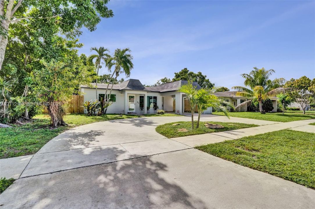 Single-story exterior featuring a hip roof, stucco facade, expansive concrete circular driveway, and mature landscaping