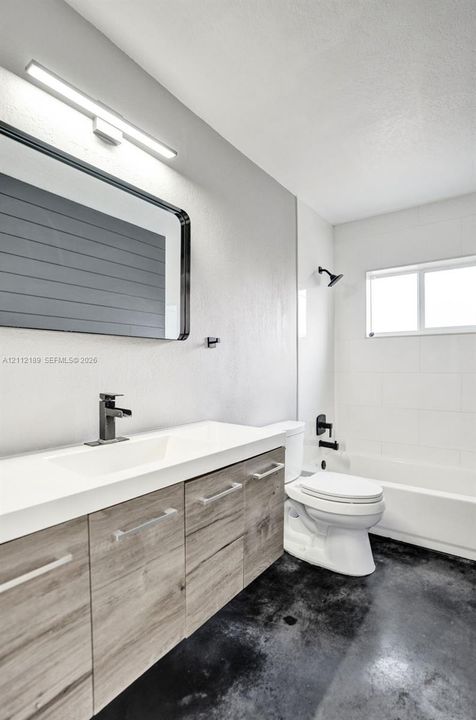 Bathroom featuring a floating wood-finish vanity with an integrated basin, matte black wall-mounted fixtures, rectangular-framed mirror, and tub-shower combination with tiled surround
