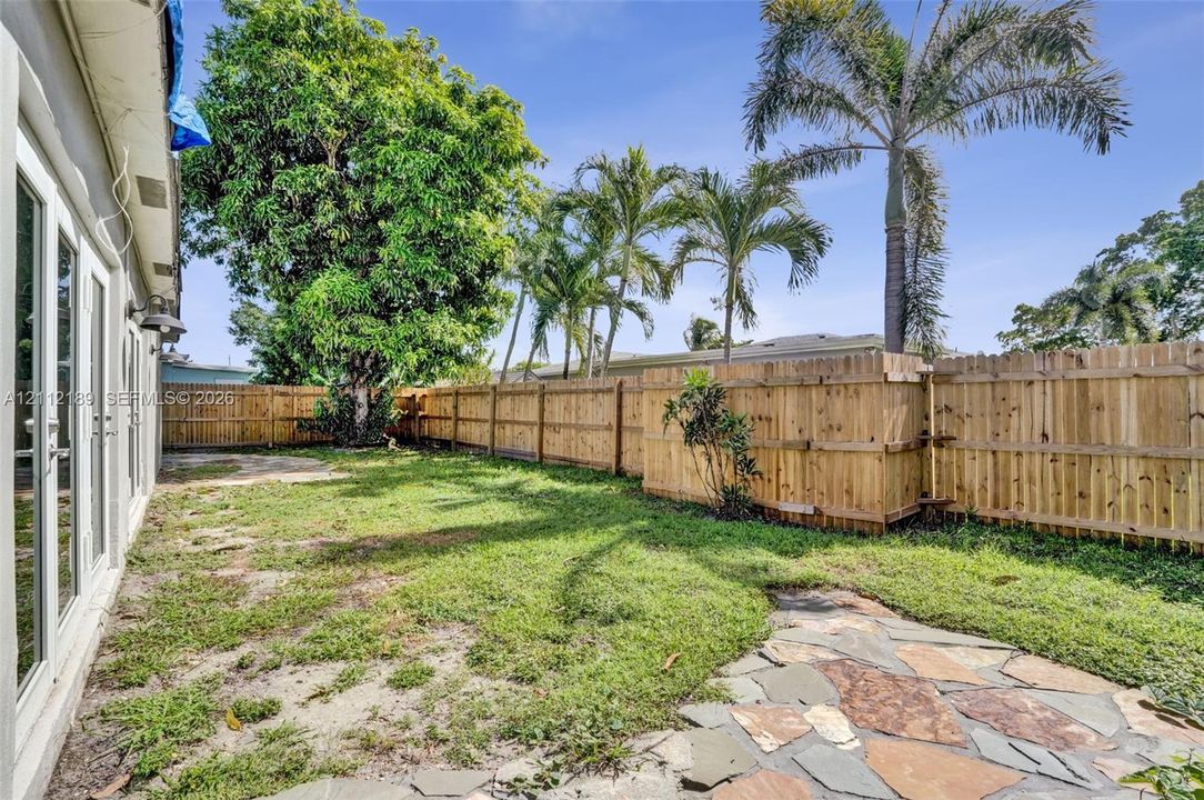 Backyard featuring a wood privacy fence, flagstone patio, lawn area, and mature palm trees