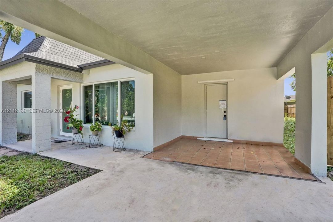 Covered carport featuring neutral-toned stucco exterior, terracotta-style tiled flooring, and multiple large windows