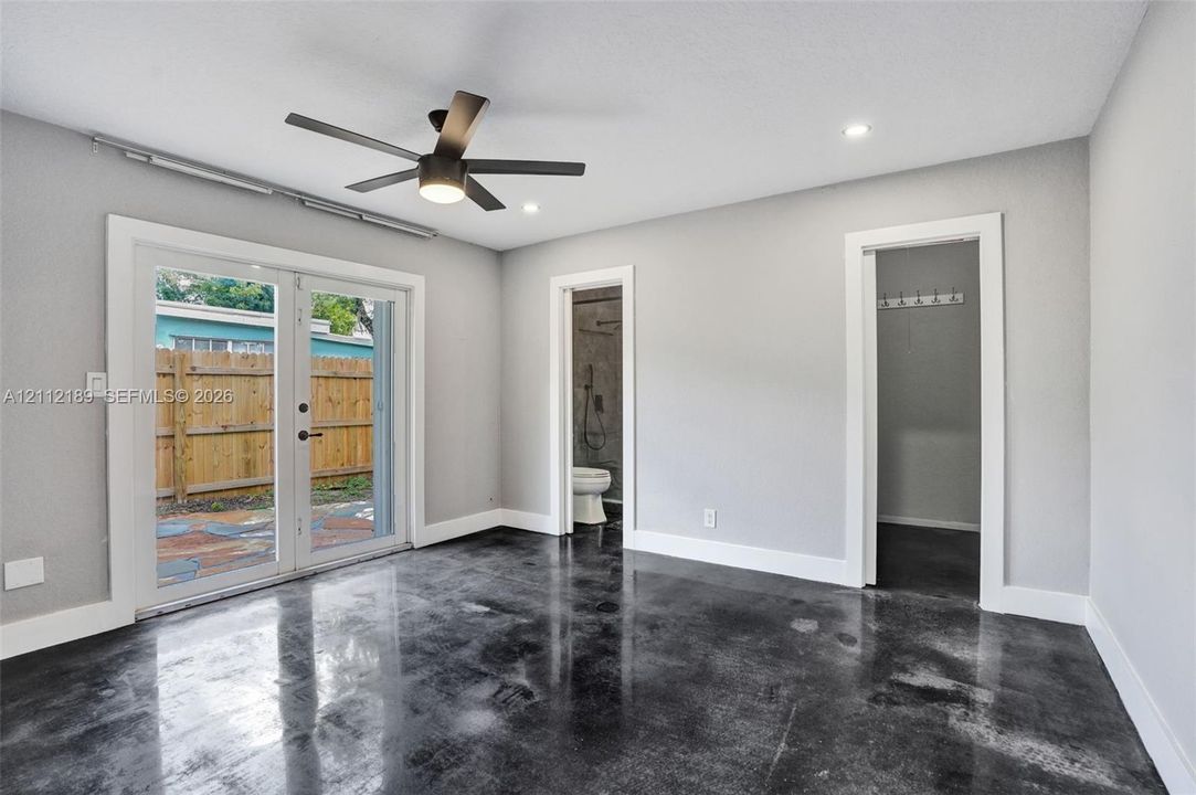 Polished concrete flooring, recessed ceiling lighting, matte black ceiling fan, and double glass-paned doors with exterior access