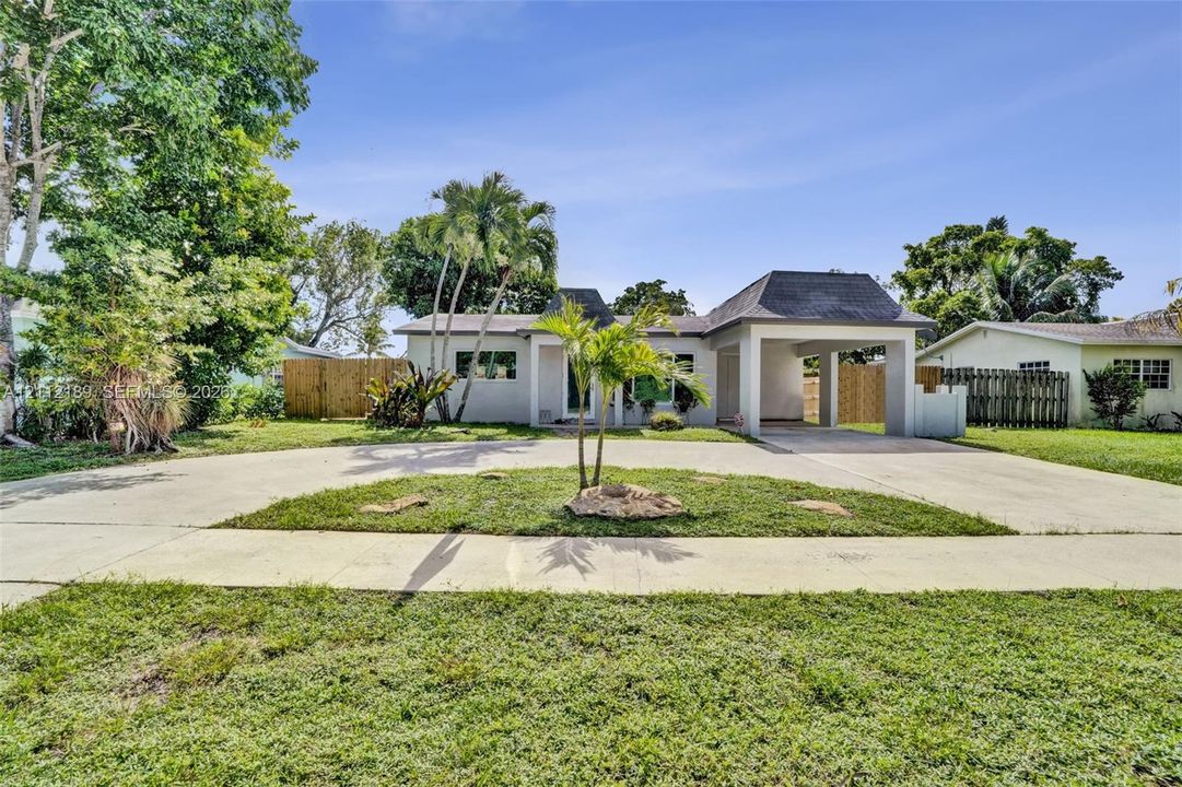 Single-story exterior featuring a hip roof, a concrete circular driveway, an attached carport, and mature palm trees