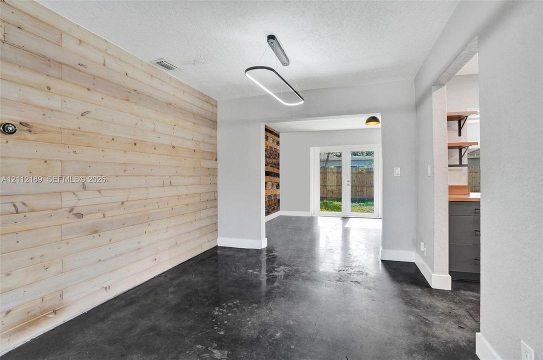 Interior space featuring horizontal natural wood-finish wall paneling, polished concrete flooring, a contemporary oval LED light fixture, and double glass-paned doors