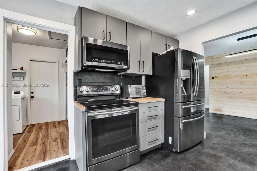 Kitchen featuring gray slab-front cabinetry, stainless steel appliances, a dark stone-finish backsplash, wood-surface countertops, and recessed lighting