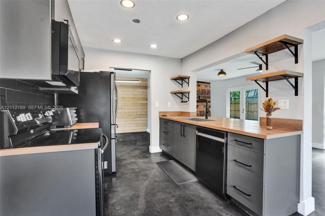 Kitchen featuring flat-panel charcoal cabinetry, wood-tone countertops, matte black hardware, recessed ceiling lighting, and open wall-mounted shelving