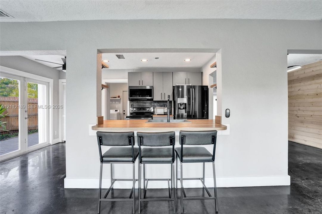 Kitchen featuring gray cabinetry, stainless steel appliances, a wood-finish countertop pass-through, and concrete flooring
