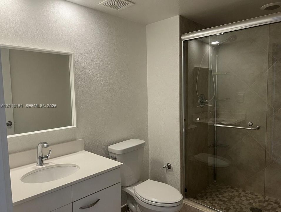 Bathroom featuring a white vanity cabinet, solid-surface countertop with an integrated basin, framed wall mirror, and a walk-in shower with a sliding glass door and tile surround