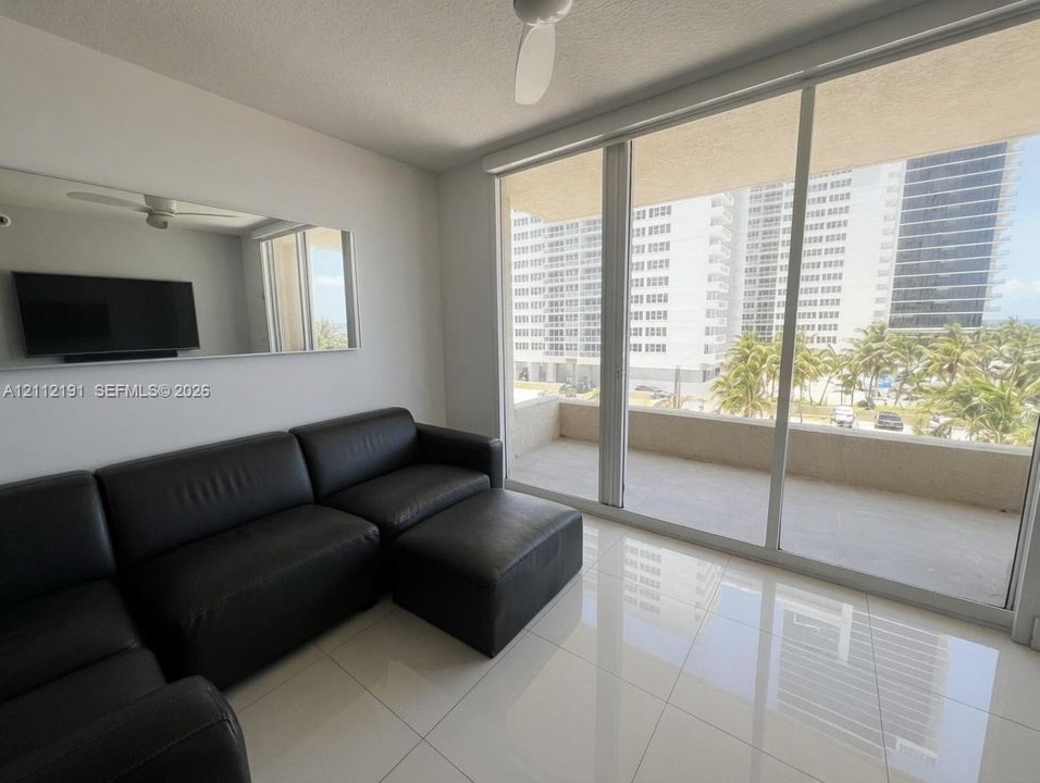 Floor-to-ceiling glass sliding doors, private balcony, polished tile flooring, built-in wall mirror, and ceiling fan
