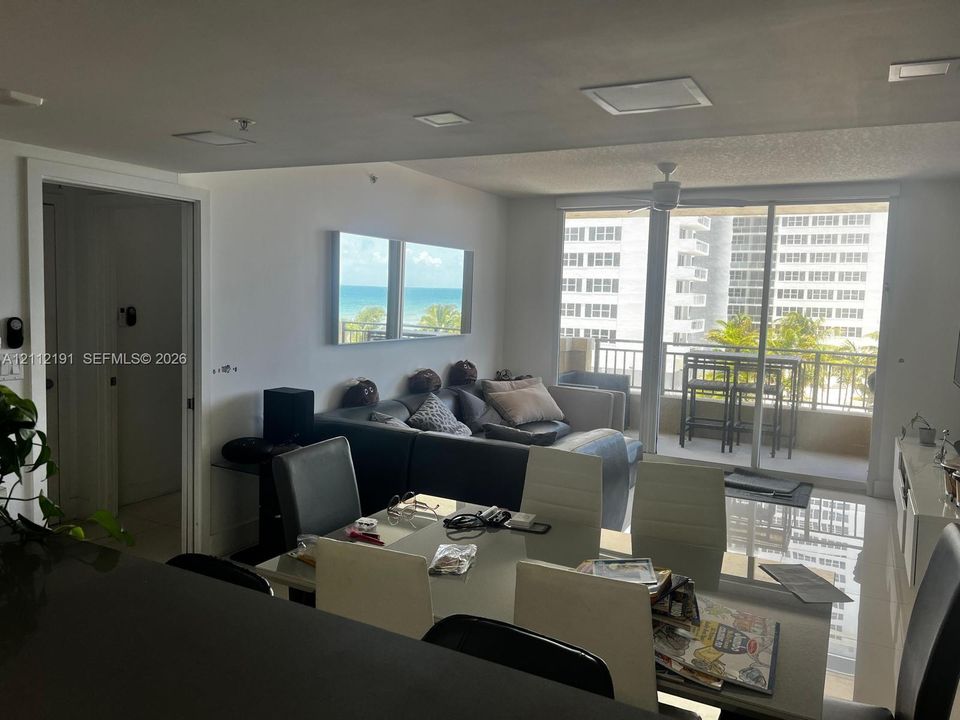 Open-concept interior featuring recessed ceiling lighting, large-format tile flooring, a balcony with a metal railing, and floor-to-ceiling glass sliding doors