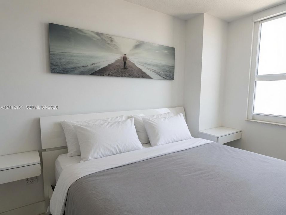 Neutral-toned interior featuring smooth wall finishes, a large multi-pane window, and dual wall-mounted floating bedside surfaces