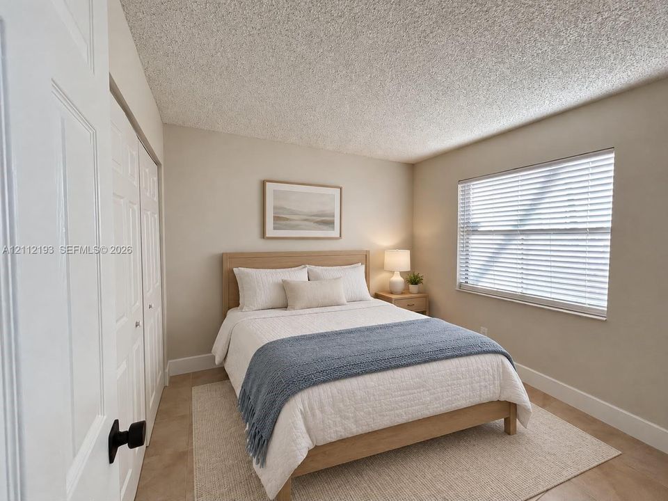 Neutral interior featuring light-toned flooring, textured ceiling, dual-panel closet doors with matte black hardware, and a window equipped with horizontal blinds